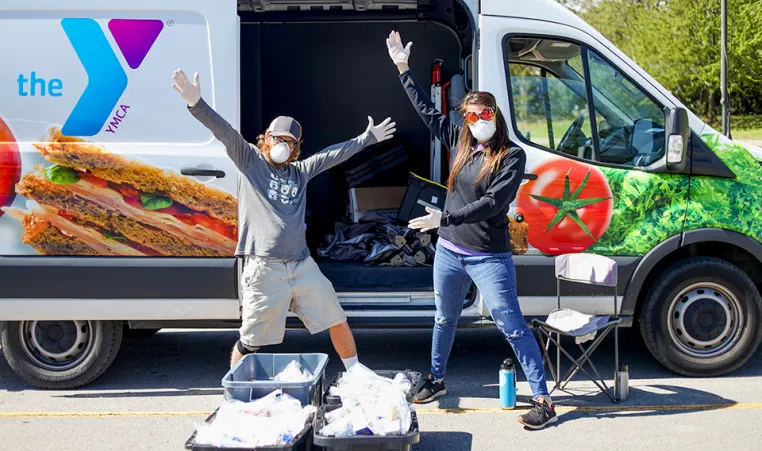Two people with food donations in front of a YMCA van