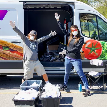 Two people with food donations in front of a YMCA van